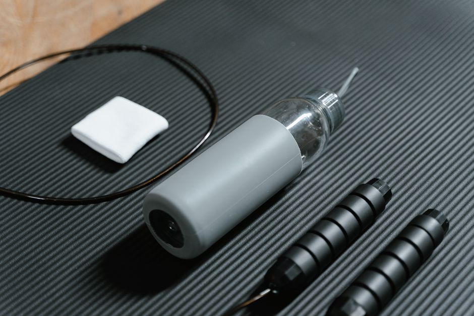 Gray water bottle and jump rope on textured black yoga mat. Indoor workout essentials.